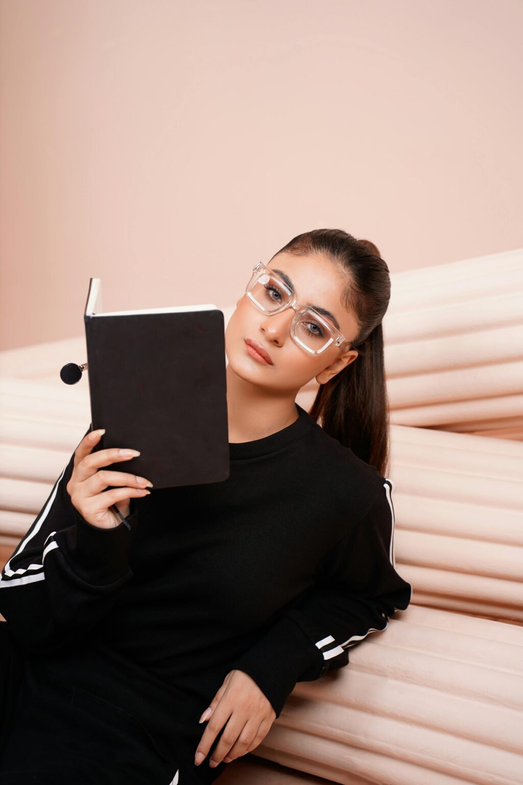 SMM A young woman in sportswear and eyeglasses reads a book indoors, exuding focus and style.