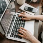 SEO From above of unrecognizable woman sitting at table and typing on keyboard of computer during remote work in modern workspace