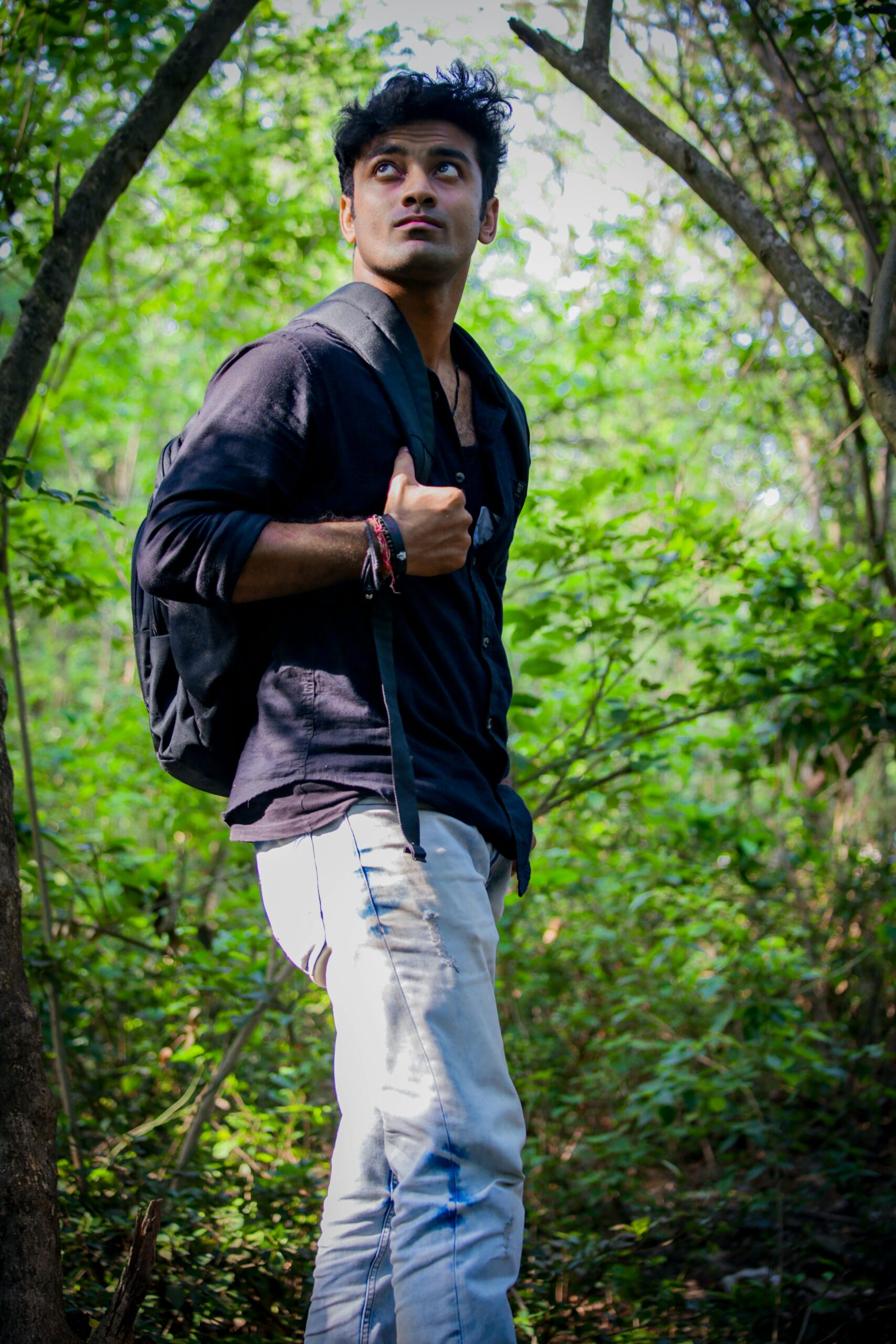 Home Casual young man with backpack exploring a green forest in daylight.