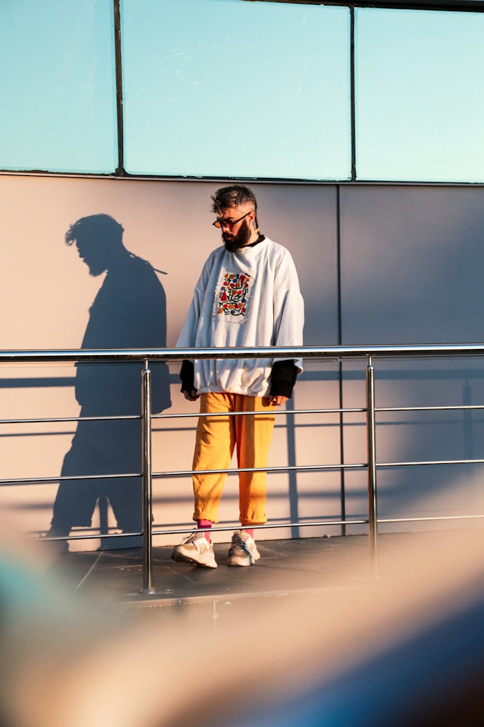 services-01 Stylish man in trendy clothes stands on a sunlit terrace casting a shadow.