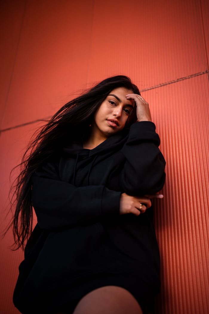 Low angle shot of a woman posing against a red wall in casual black attire.