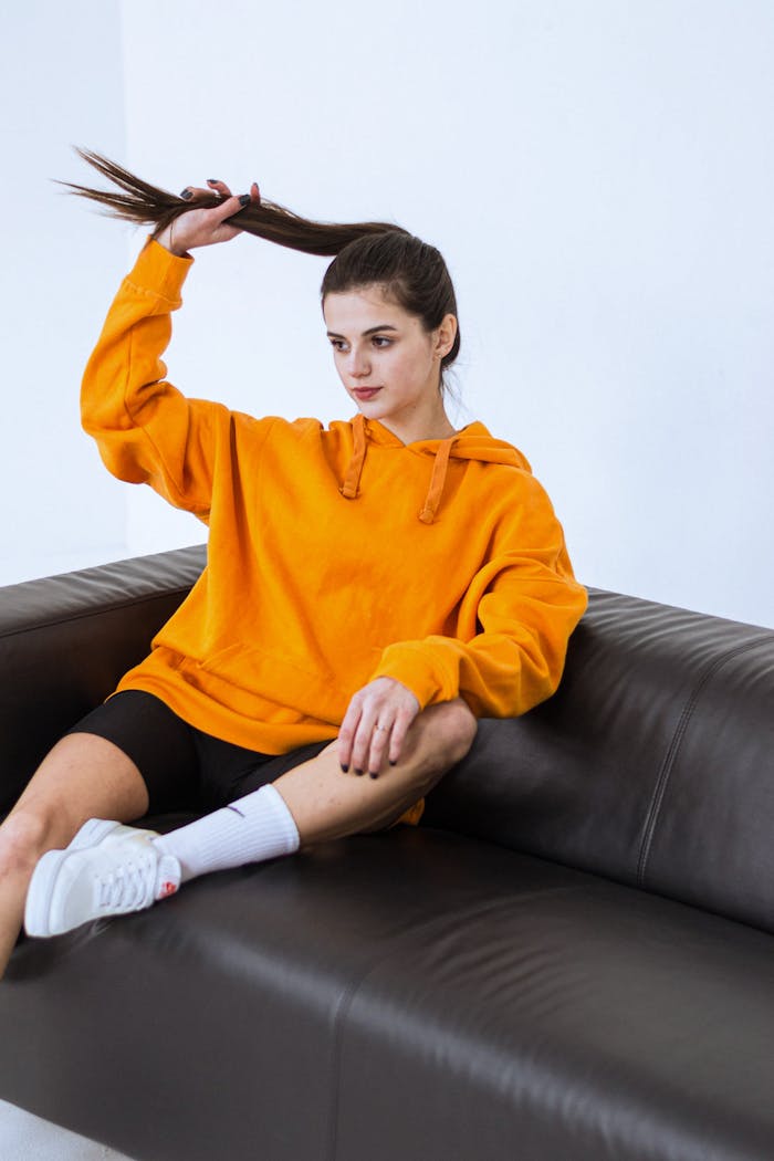 Young woman posing in an oversized orange hoodie on a sofa, capturing a casual and trendy style.