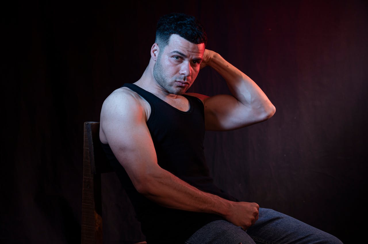 Muscular man in a black tank top posing dramatically against a dark backdrop.