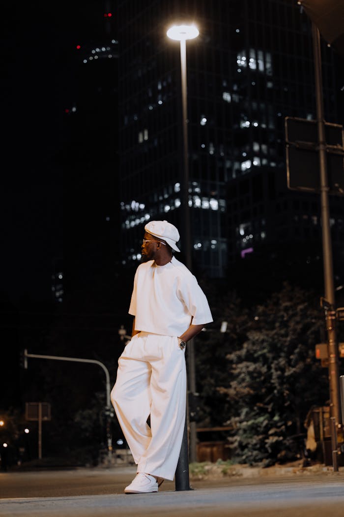 Stylish person in white outfit posing under city streetlights at night.