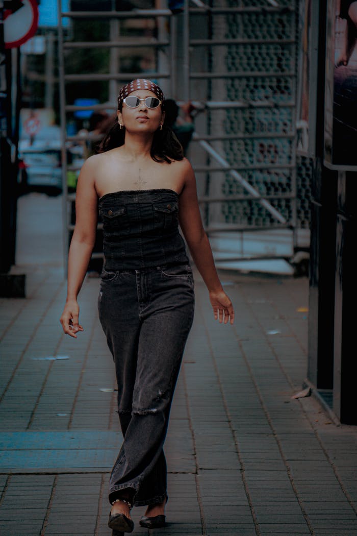 A fashionable woman with sunglasses and headband walks confidently down an urban sidewalk.