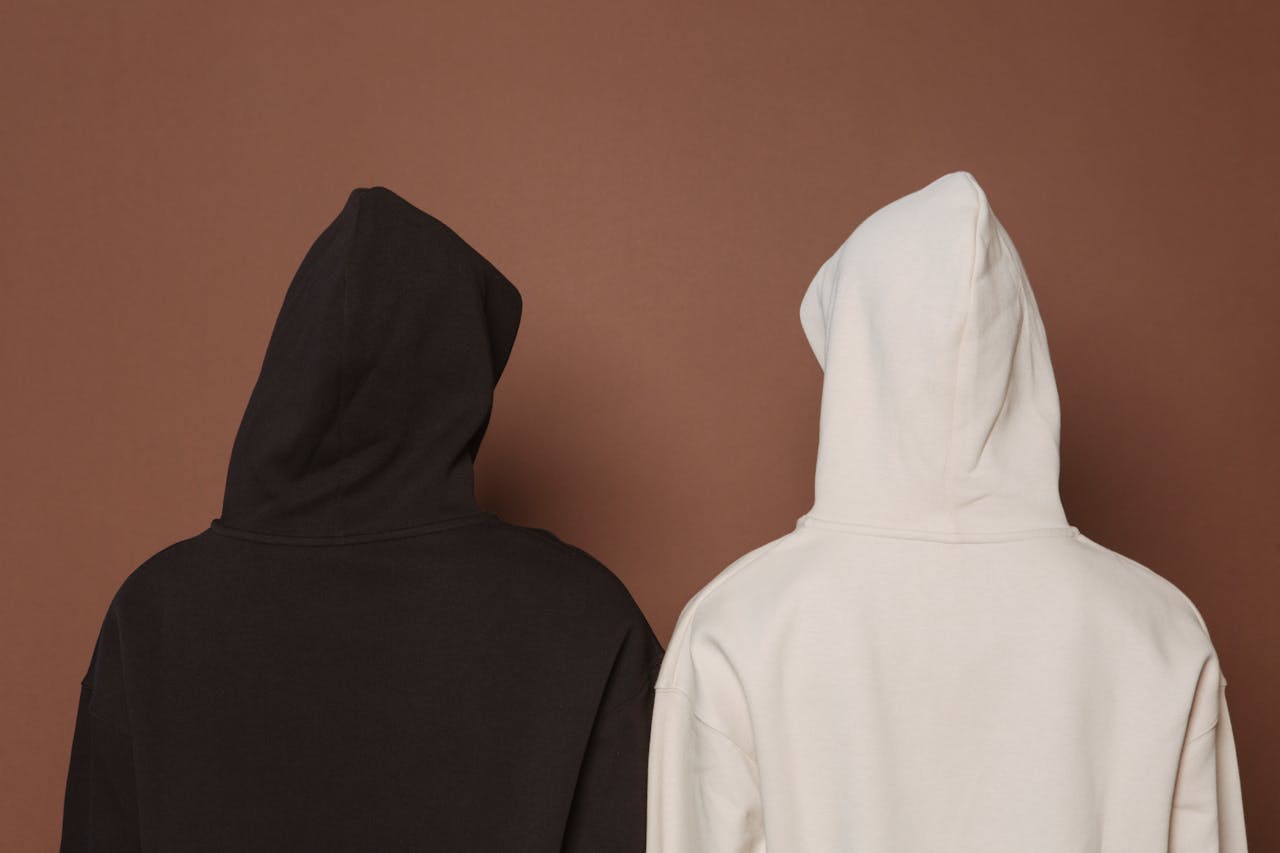 Back view of anonymous models in similar oversize hooded sweatshirt standing against brown background