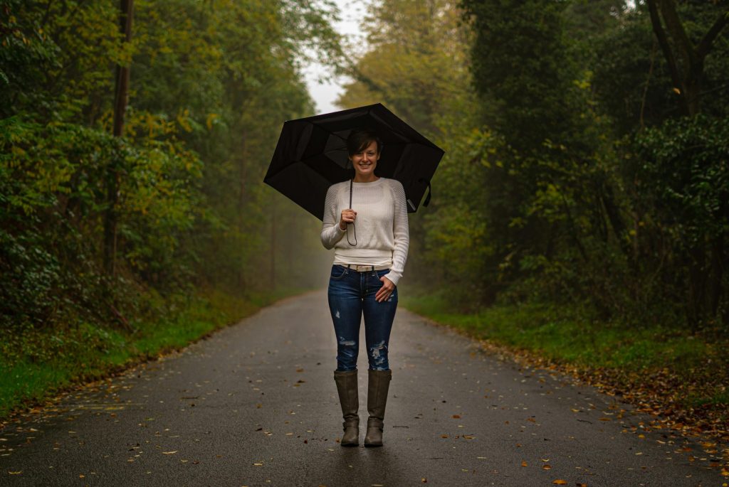 pexels-photo-3836252-3836252 A young woman in a white sweater holding an umbrella on a foggy autumn road.