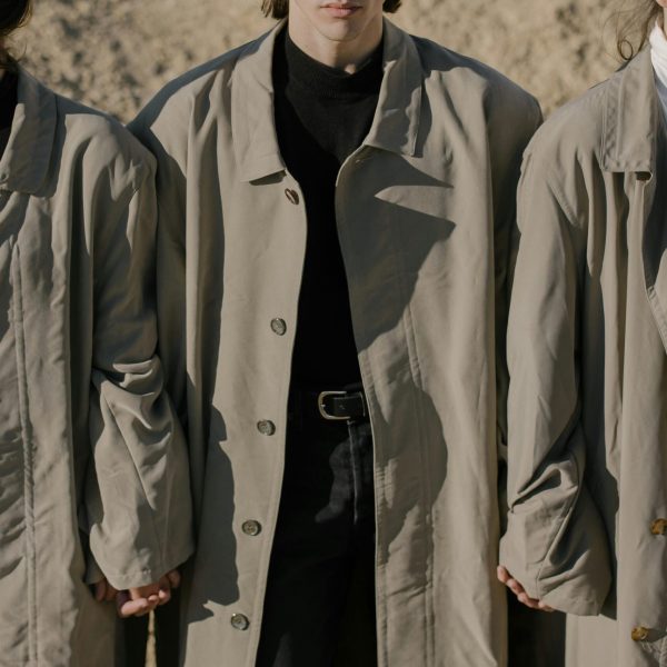 Three stylish adults in trench coats exude urban fashion chic as they hold hands outdoors.